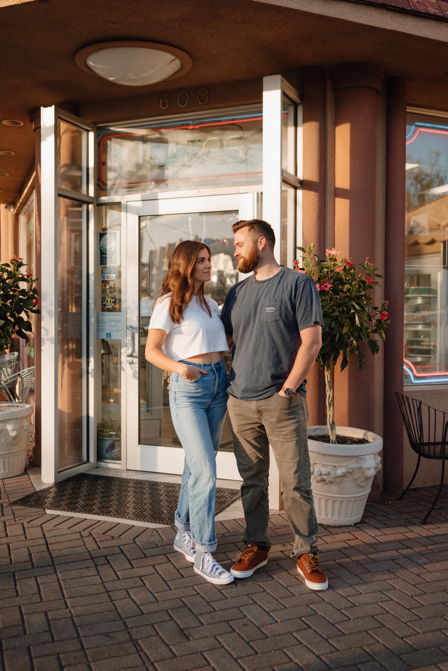 woman and man couple posing for laidback engagement session outside a bakery entrance wearing jeans and t-shirt