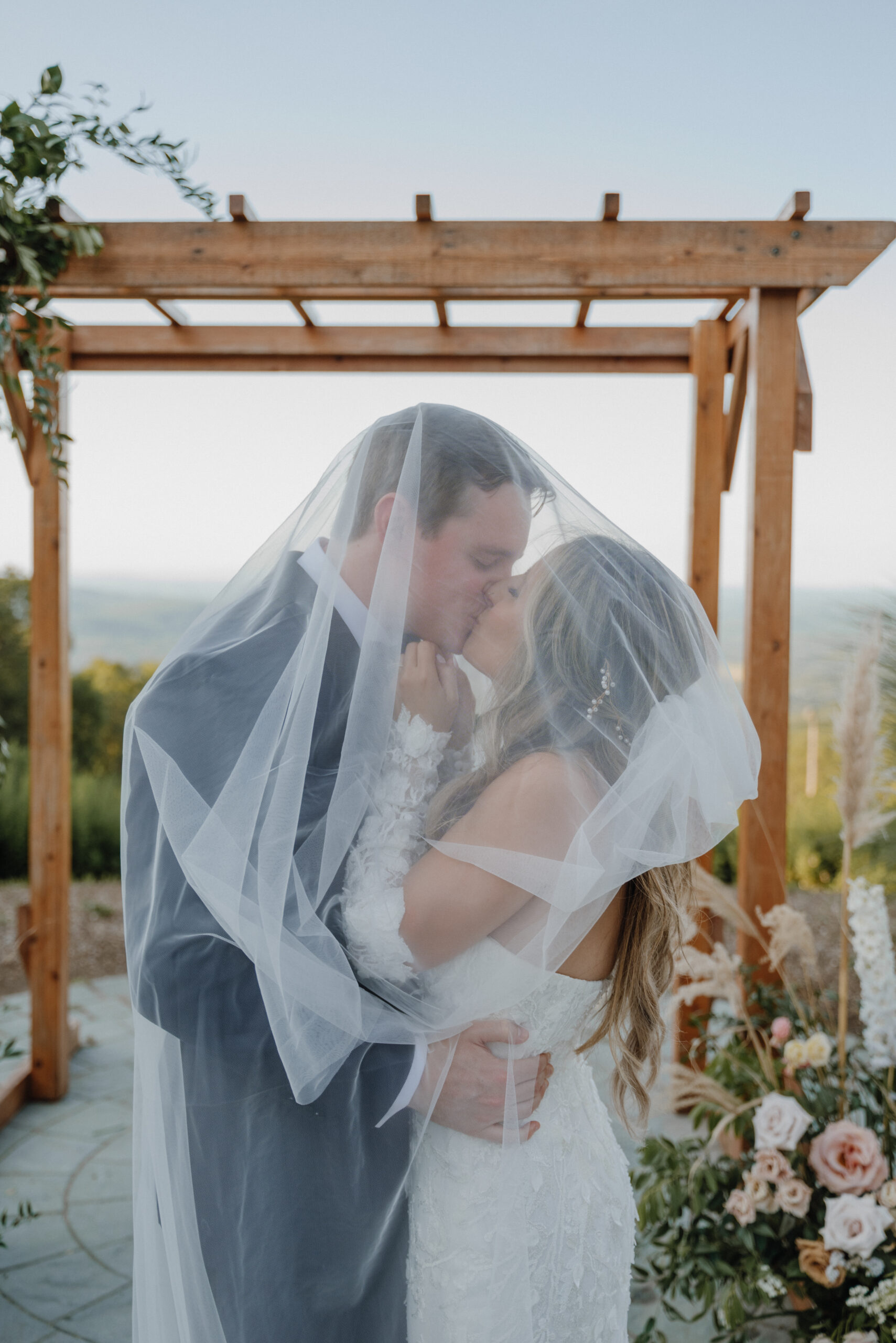 couple on their wedding at the top of a mountain in front of their ceremony arch kissing under the brides veil