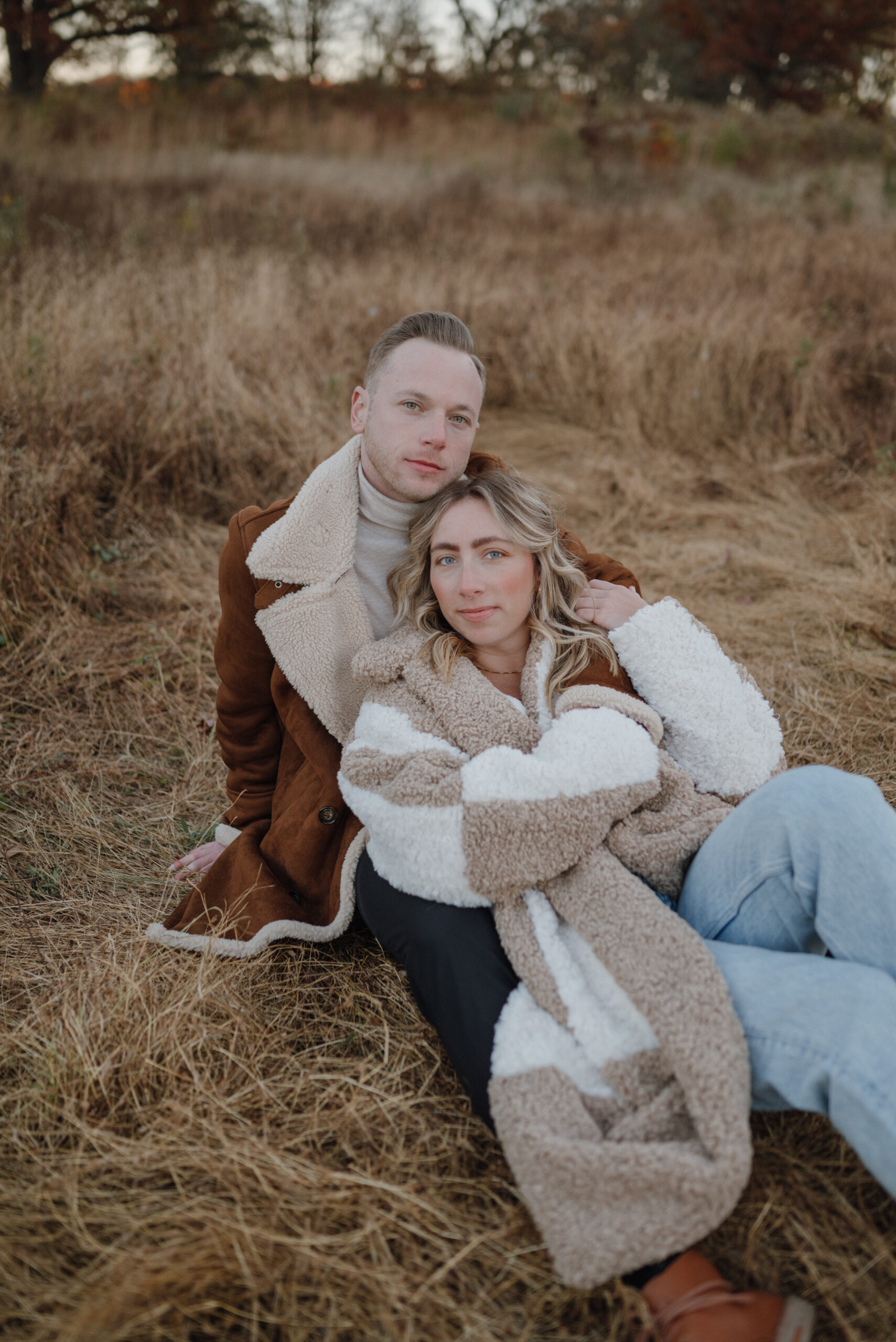 Woman and Man couple laying in the grass in western boho fall/winter attire with oversized jackets for couples photos